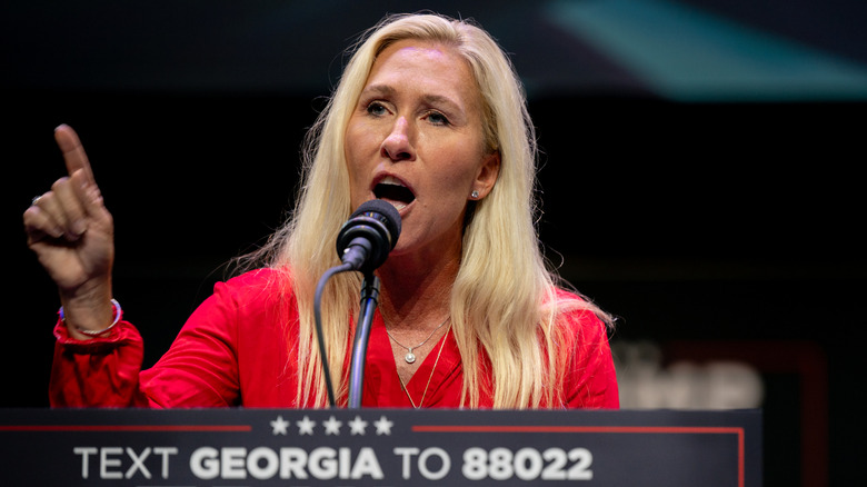 Marjorie Taylor Greene giving a speech in a red shirt while raising a finger