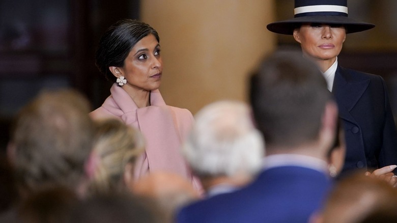 Usha Vance wearing a pink coat standing next to Melania Trump who's wearing a black and white hat and a black trench coat.