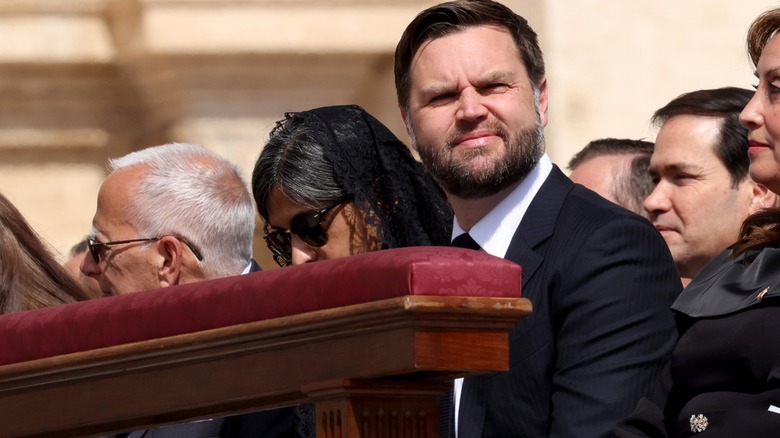 Usha Vance wearing a veil and sunglasses with her head down next to JD Vance who's smiling.
