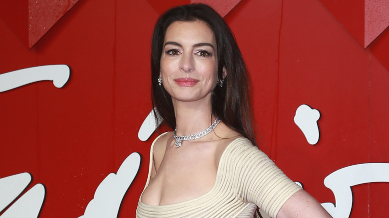Anne Hathaway smiling in a white dress at the Fashion Awards.