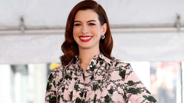 Anne Hathaway smiling in a pink and green dress