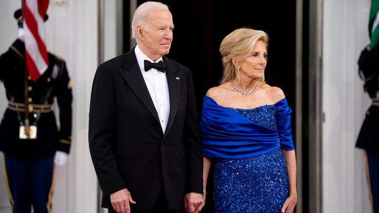 Joe Biden and Jill Biden in formal attire holding hands outside White Hands