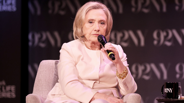 Hillary Clinton giving a speech onstage in a beige ensemble