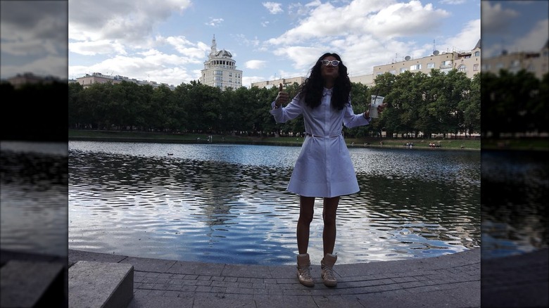Elena Moussa posing with a coffee in hand in front of a body of water.