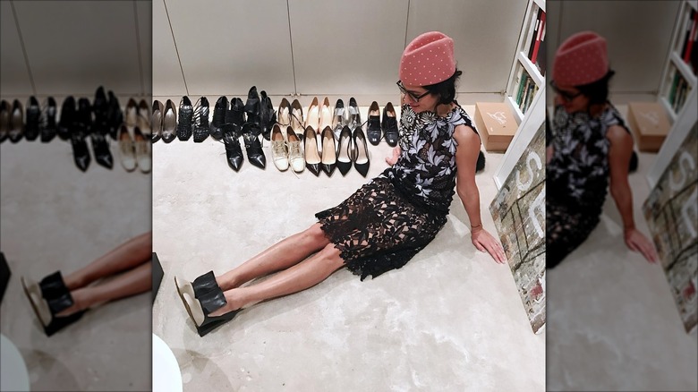Elena Moussa sits on the floor in a pink hat, surrounded by shoes.