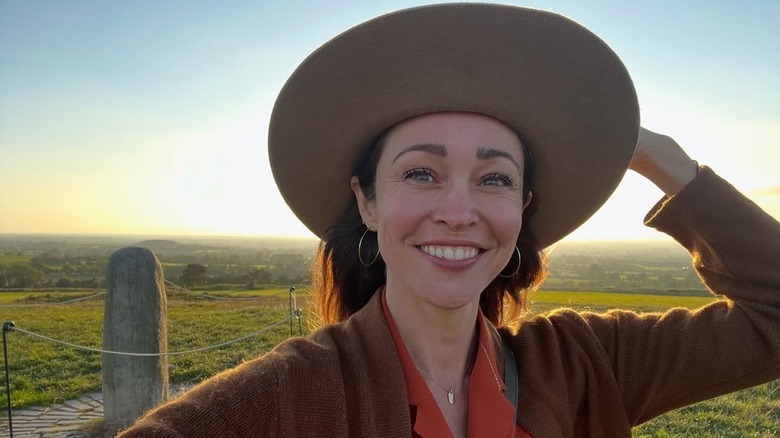 Autumn Reeser wearing a statement hat, orange top, and brown sweater