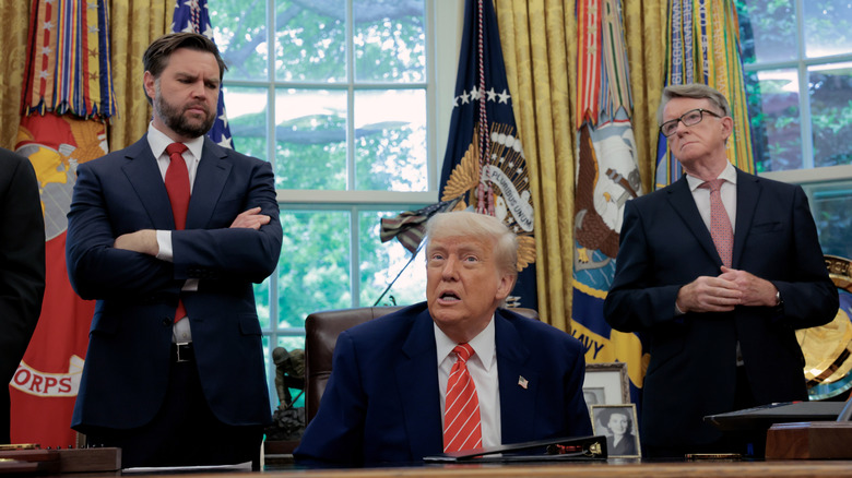 JD Vance standing beside President Donald Trump with his arms crossed, in the Oval Office.