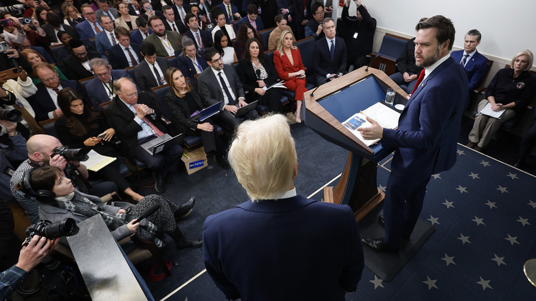 In the White House Press room, JD Vance takes to podium in a crowded room, glaring over at Donald Trump.