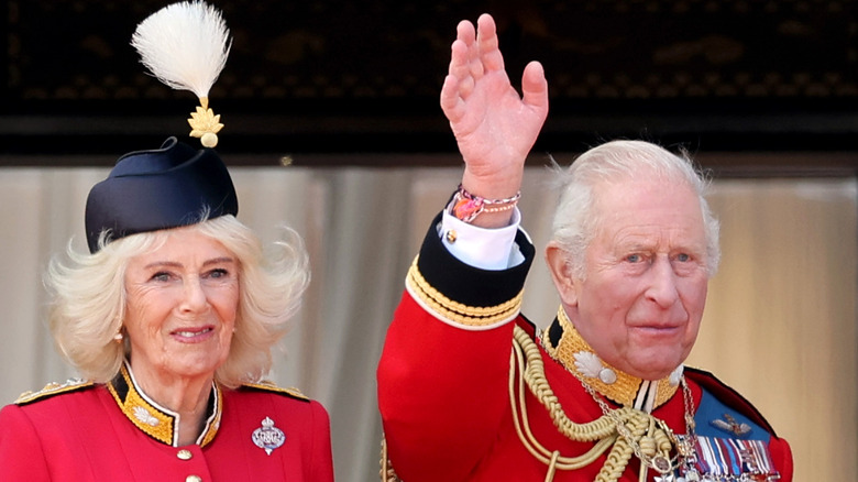 Queen Camilla smiling next to King Charles III waving