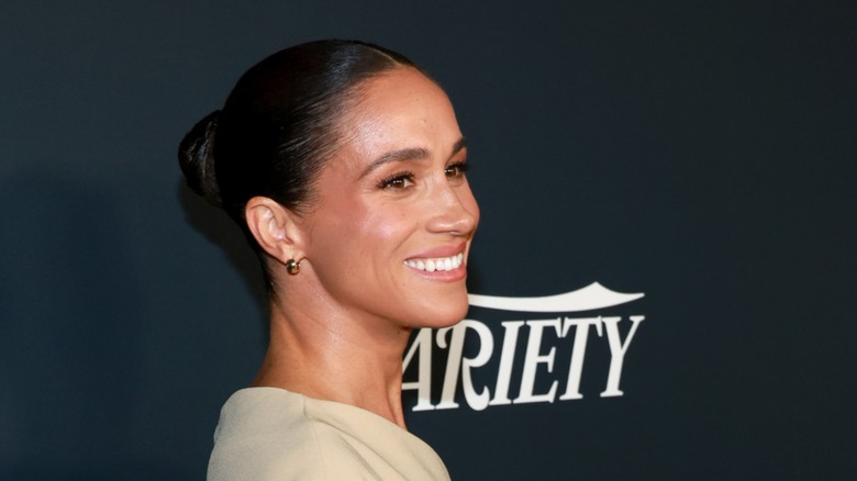 Meghan Markle smiling on the red carpet in a cream off the shoulder dress