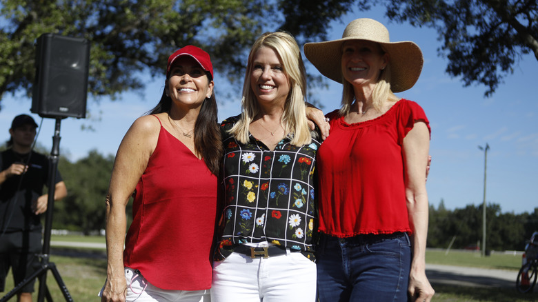 Pam Bondi outside in the sun with two women in red.