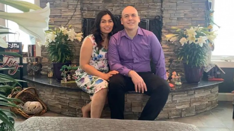 Jeremy Taylor and wife, Kim Taylor sitting on the brick of a fireplace.