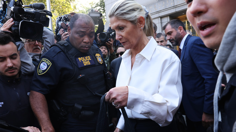Nadine Menendez swarmed by police and press as she walks out of stone building.