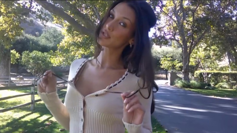 Bella Hadid in cream sweater with black ribbon standing outside