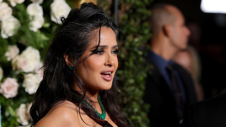 Salma Hayek in front of flowers wearing green necklace