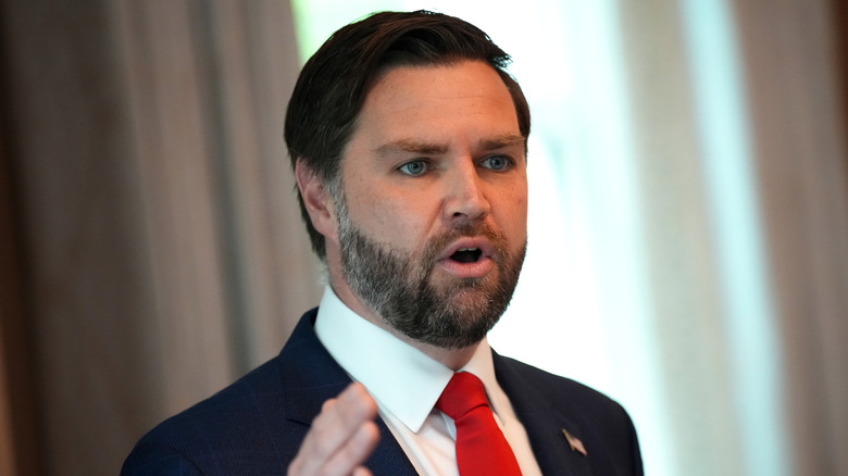 JD Vance, gesturing while talking, in a suit with a red tie.