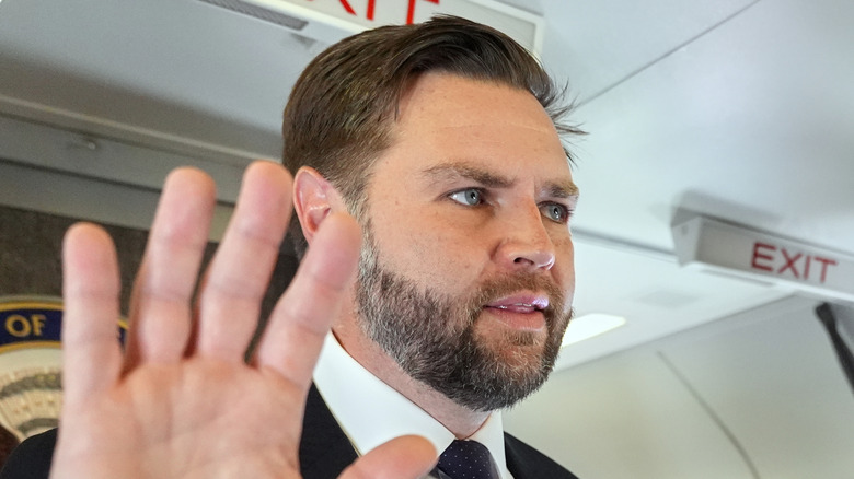 JD Vance, his hand held up to partially block camera, looks off to the right.
