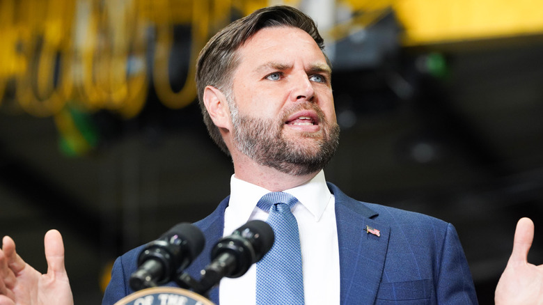 JD Vance from a low angle while he gestures behind a microphone.