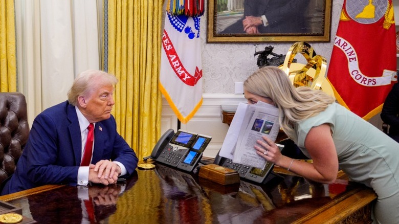 Karoline Leavitt leans to whisper to Donald Trump inside the Oval Office of the White House (2025)