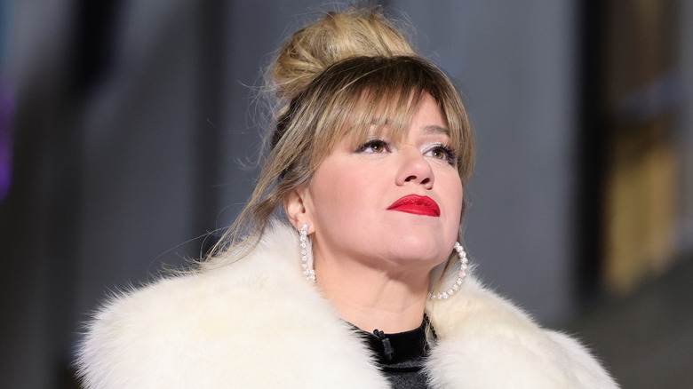 Kelly Clarkson wearing a high bun and a red lip with a fuzzy coat