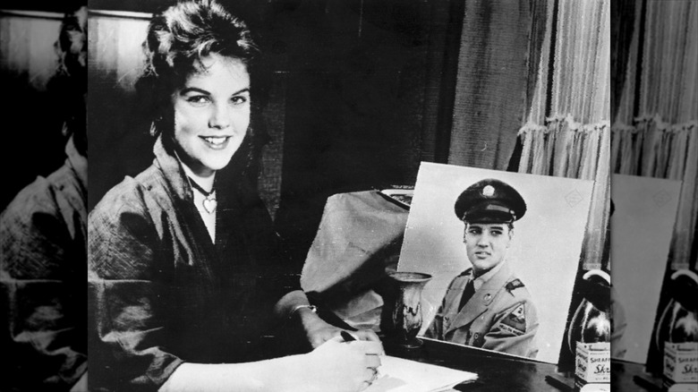 Priscilla Presley writing a letter to Elvis Presley next to a portrait of him in uniform.