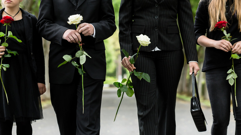 four people walking in a cemetery while carrying roses