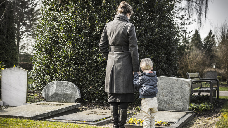 a mother and her 4 year old son stand in front of a gravestone