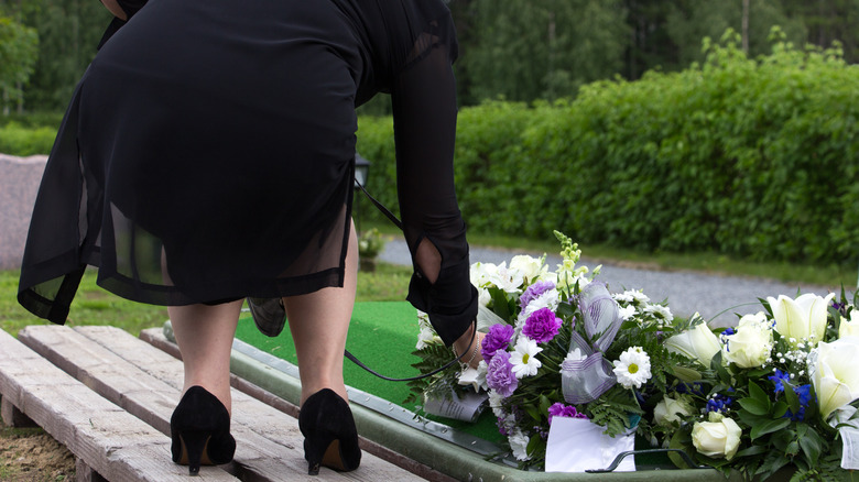 a woman placing flowers on a fresh grave