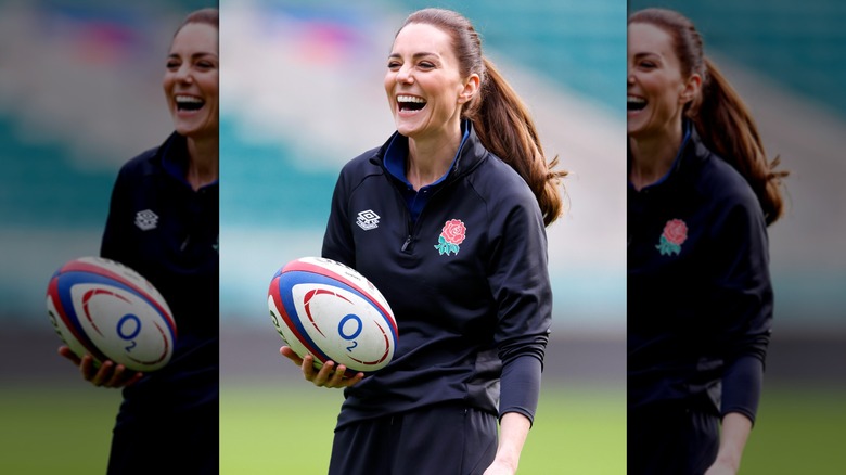 Kate Middleton smiles in a navy blue jacket and track pants.