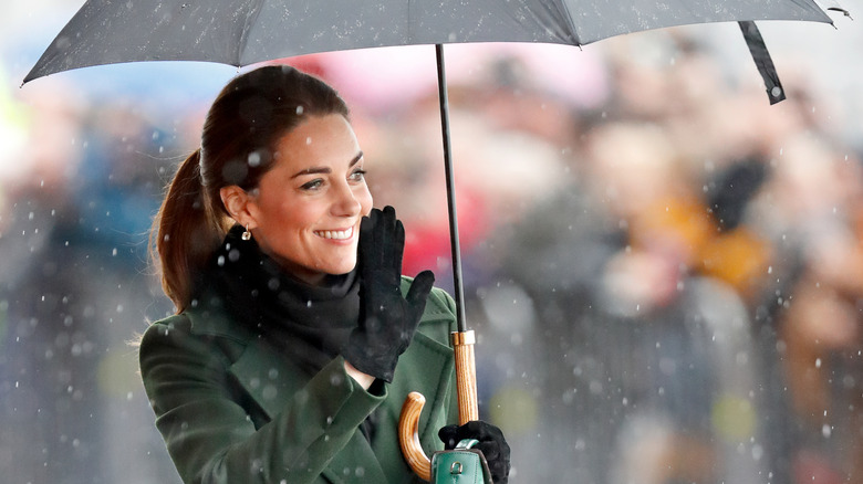 Kate Middleton smiles and waves while holding an umbrella