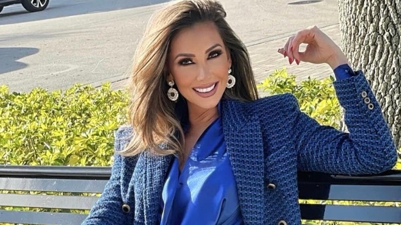 Katrina Campins poses on a park bench in a blue suit (2025)