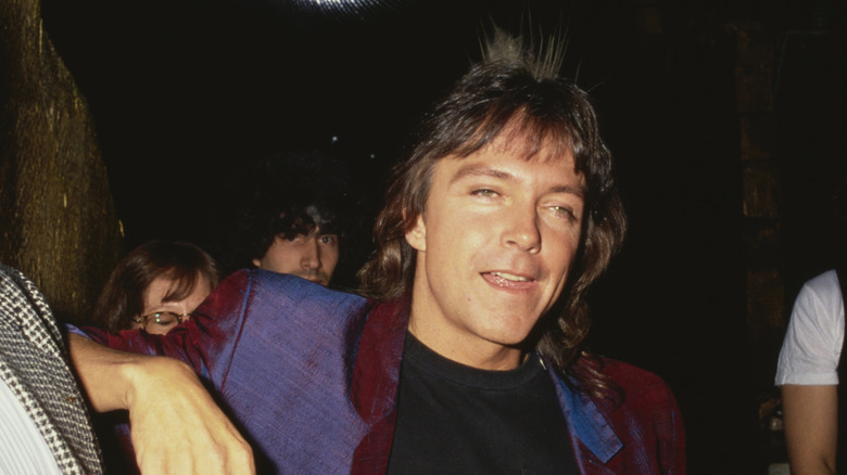 Nighttime candid photo of David Cassidy with several people partially visible behind him in the dark.