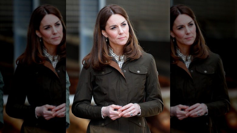 Kate Middleton tilting her head in a dark green jacket on a farm.