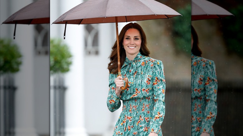 Kate Middleton smiles holding an umbrella.