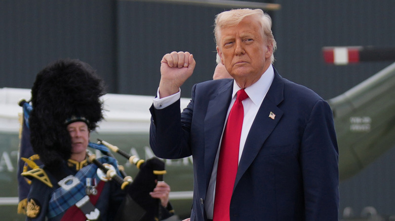 Donald Trump raises a pale fist to his face.