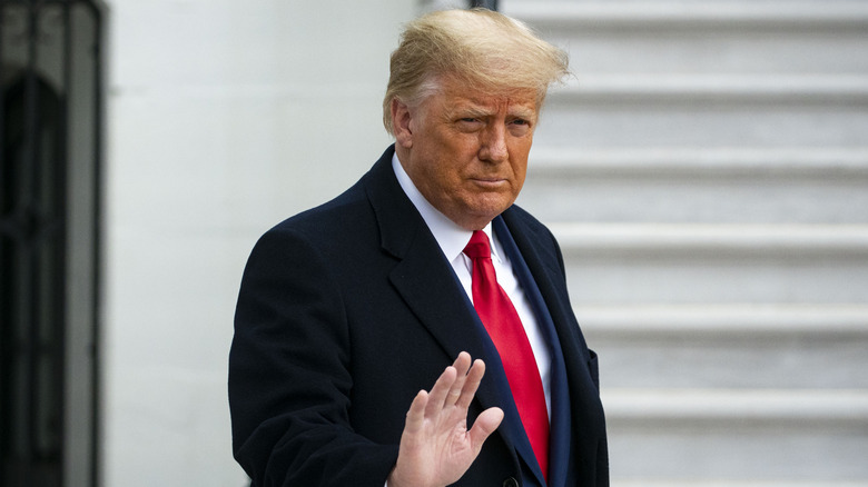Donald Trump with his hand raised in front of white stairs.