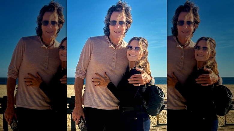 Rick Springfield hugging his wife Barbara in front of a beach and ocean