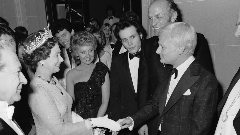 Queen Elizabeth II shakes hands with English comic actor John Inman at the Royal Variety Performance, London, 1981. Left to right: Queen Elizabeth II, singers Alvin Stardust, Lulu and Adam Ant, boxer Henry Cooper and John Inman.