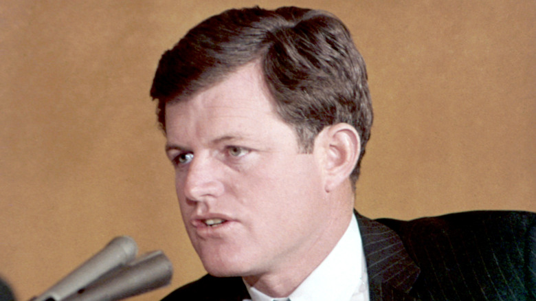 Ted Kennedy in a black suit and white shirt talking into a microphone