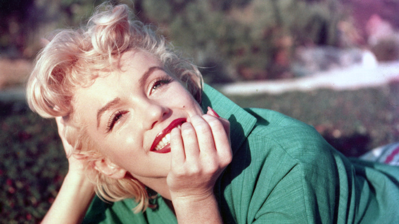 Marilyn Monroe lying in the grass in a green shirt smiling