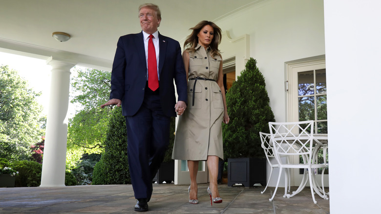 Melania Trump holds hands with Donald Trump and looks down while walking down the Rose Garden colonnade.
