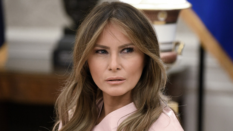 Melania Trump directs her gaze to the side and slightly parts her lips.