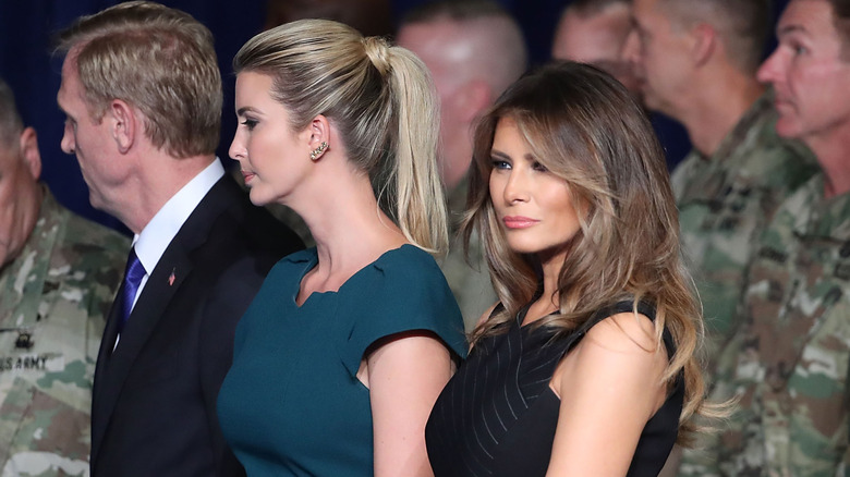 Melania Trump stands beside Ivanka Trump and smiles with members of the military behind them.