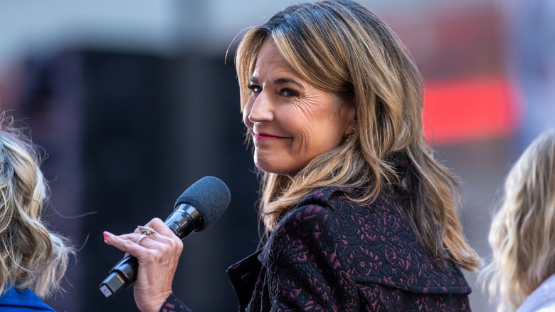 Savannah Guthrie holding a microphone while smiling.