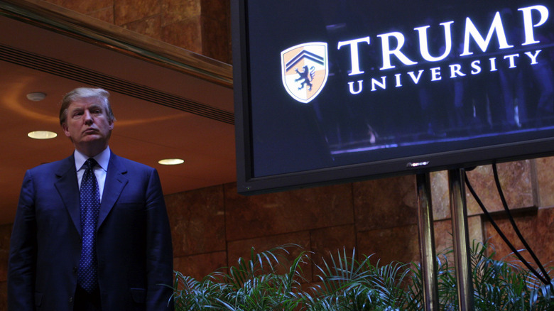 Donald Trump posing next to a screen advertising Trump University