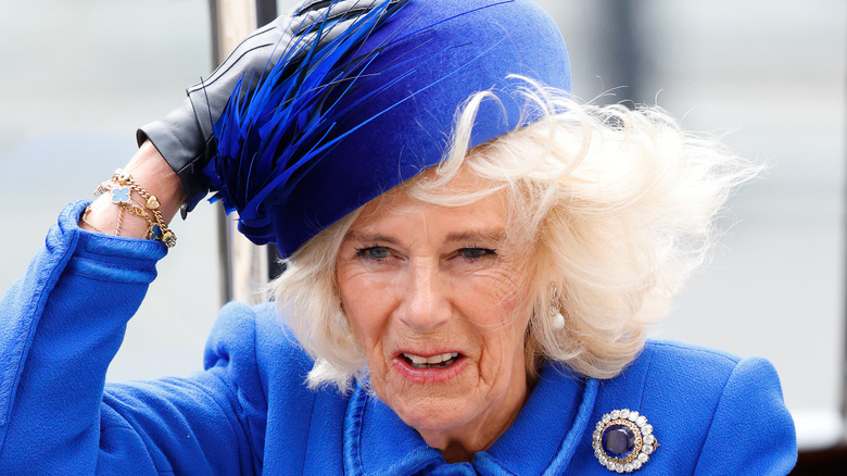 Queen Camilla holding onto her hat in the wind