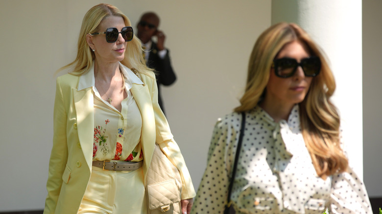Pam Bondi walking in a yellow suit with sunglasses and a patterned shirt