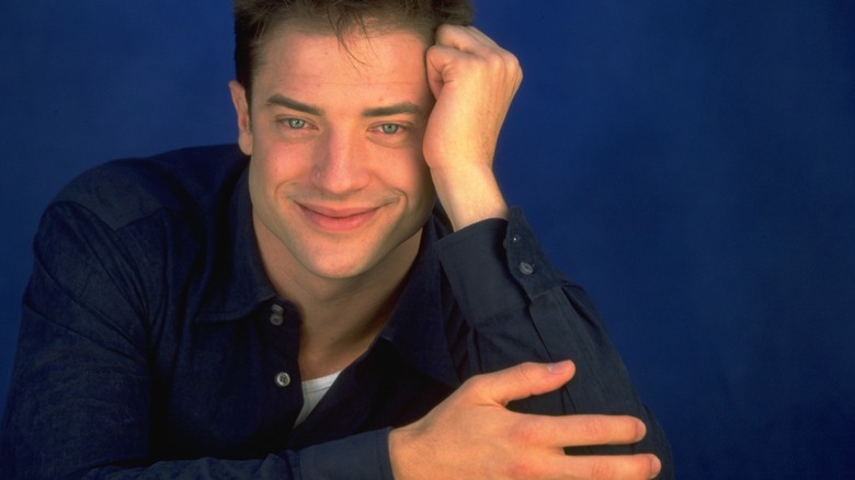 Brendan Fraser in the '90s smiling while leaning his head on his hand