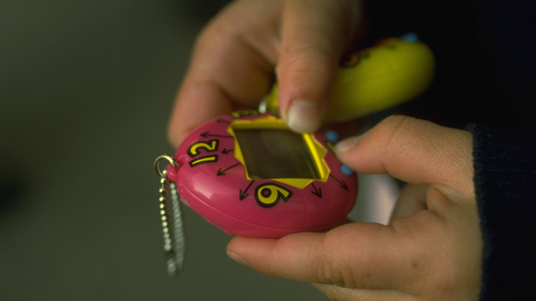 A person's hands playing on a pink Tamagotchi.