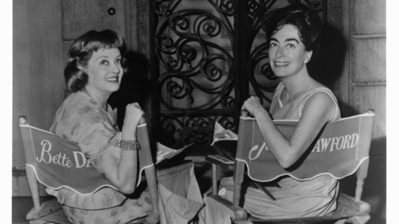 Joan Crawford and Bette Davis smiling in chairs with their names on them